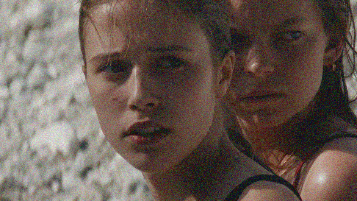 Close-up of two teen girls facing forward but looking off-camera right. The one in front covers a quarter of the other's face.