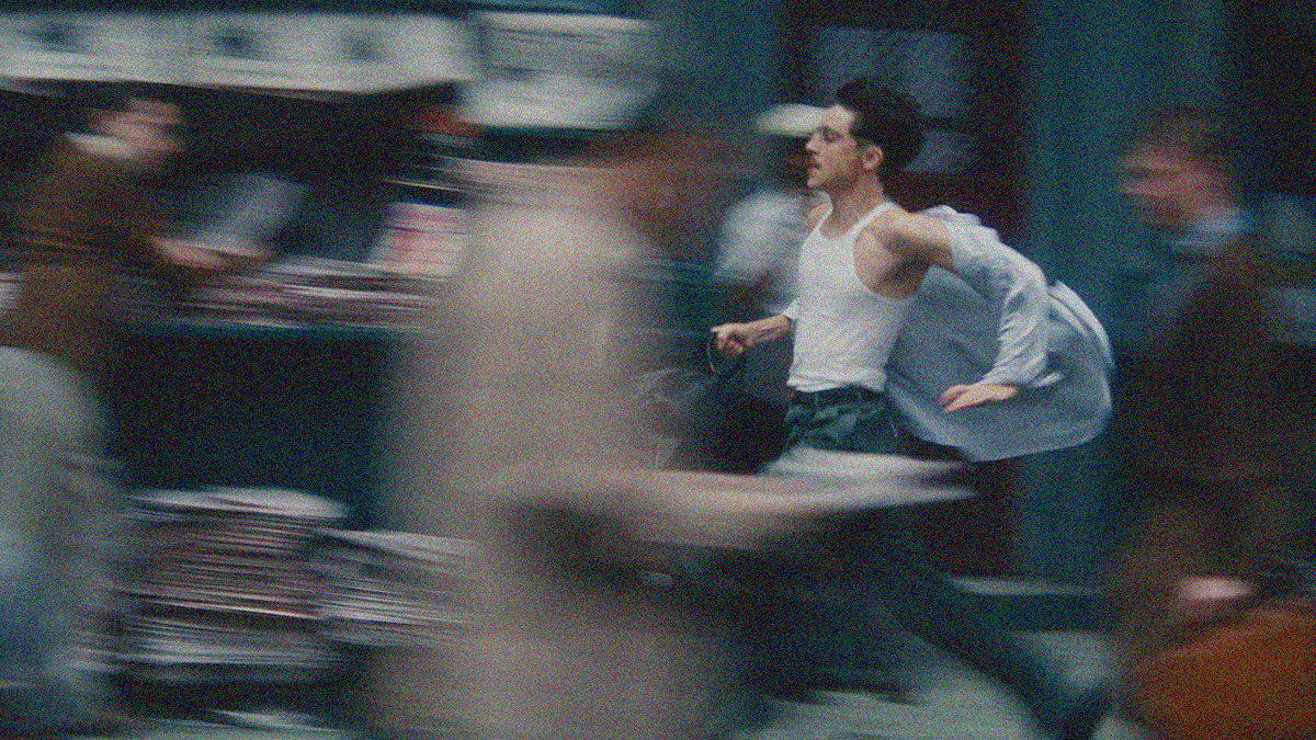 A man with glasses and mustache runs right to left in a white tank top with shirt flowing behind him. Everything else is blurred to show the speed.