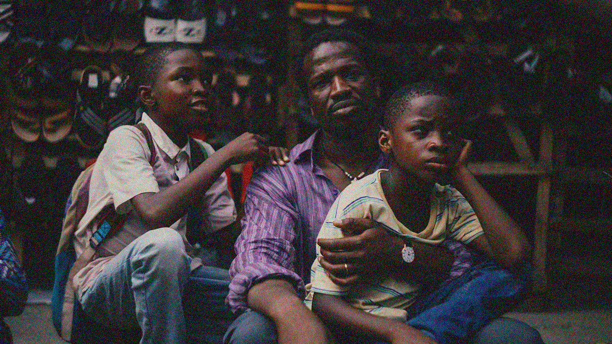 A father and his two sons sitting with a shelf of sandals behind them.