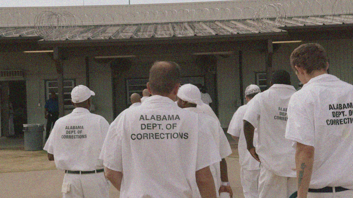 A group of men in white collared "Alabama Dept. of Corrections" walking back into their prison from outside.