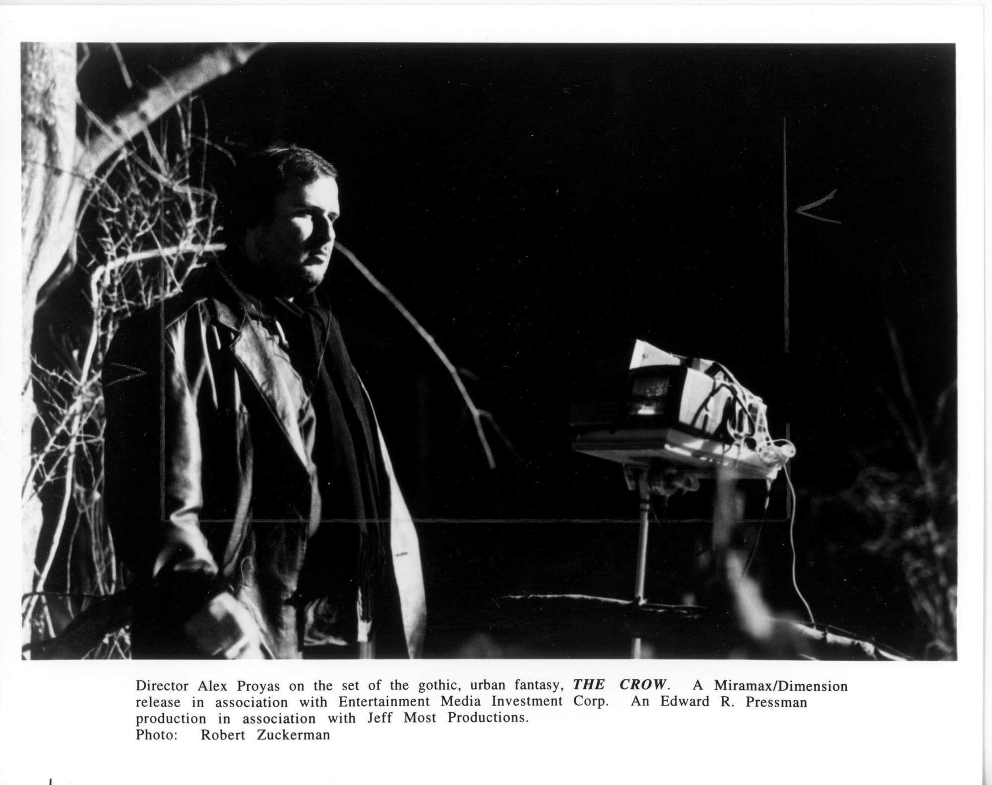 Director Alex Proyas stands at left, a barren tree behind him, wearing a leather jacket. A monitor is to his right.