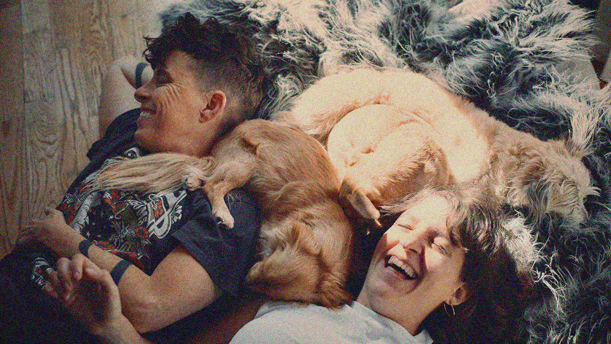 Overhead shot of two people laughing with their two dogs curled up between their heads as a beam of light shines down.