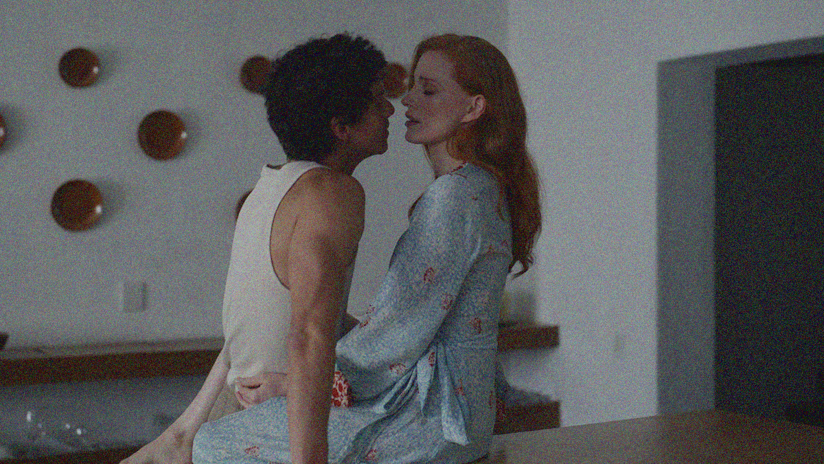 A woman seated on a kitchen counter and man standing between her legs move in for a kiss.
