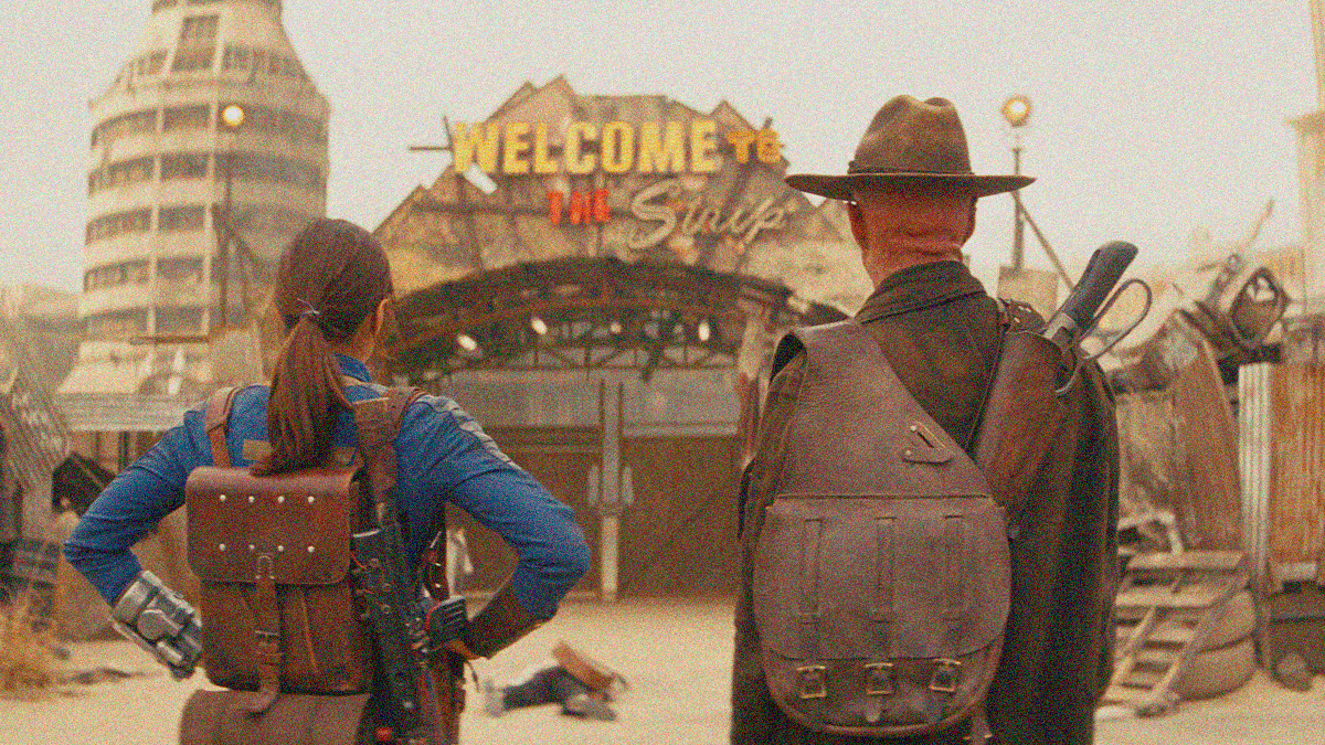 Shot from behind: a woman in blue coveralls and a back pack with hands on hips stands next to a man with cowboy hat and satchel, both staring at a gate with the neon words "Welcome to the Strip" above it.