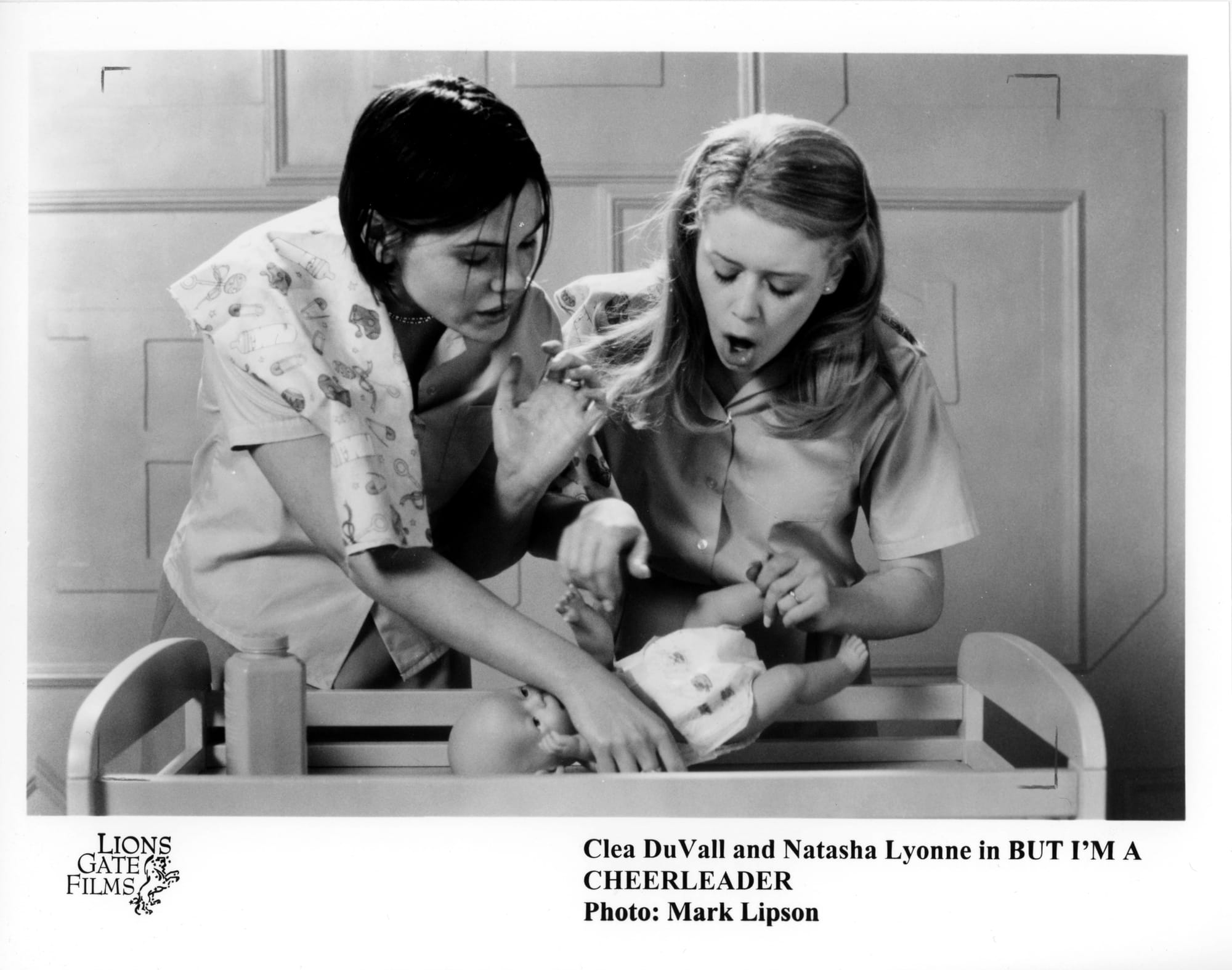 B&W Publicity Photo - Two women poorly attempt to take care of a plastic baby doll on a changing table.
