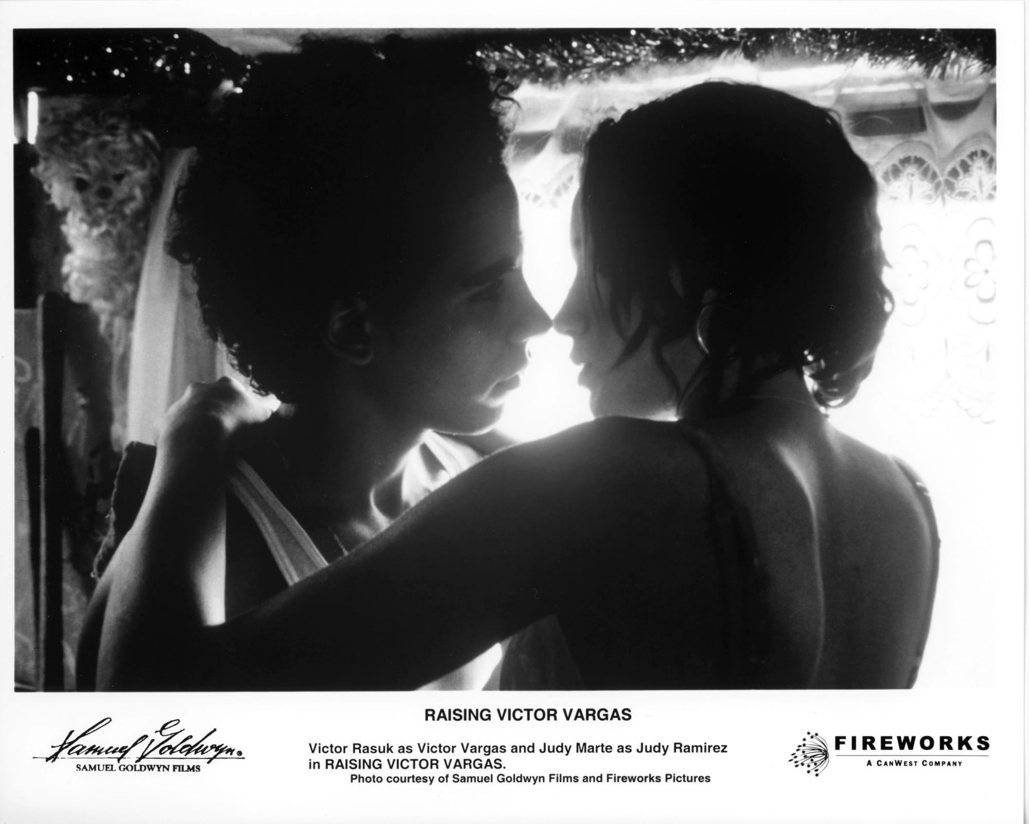B&W Publicity Photo: Shot in close-up from chest up, a young man and woman (her hands on his shoulders) lean in for a kiss.