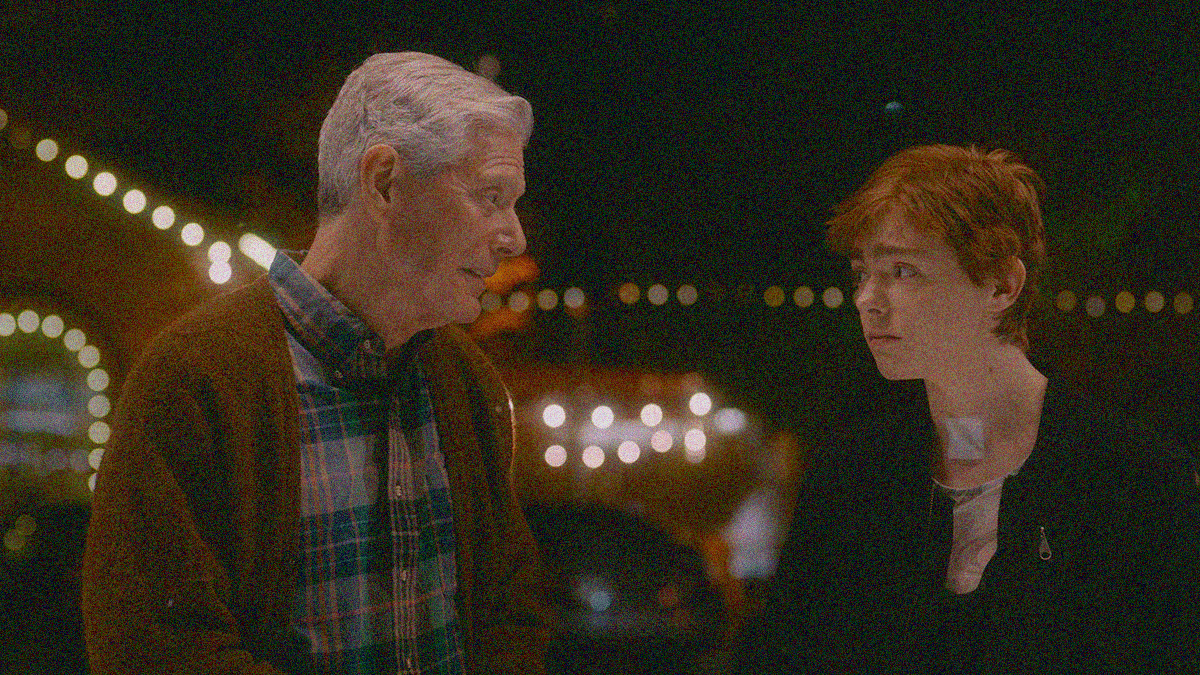 An older man in sweater at left talks with a young woman at right with a bandage on her neck.