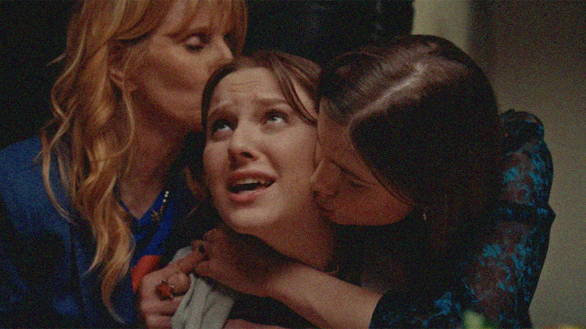 Close-up of a woman in distress being hugged and kissed on the head and cheek by two others, respectively.