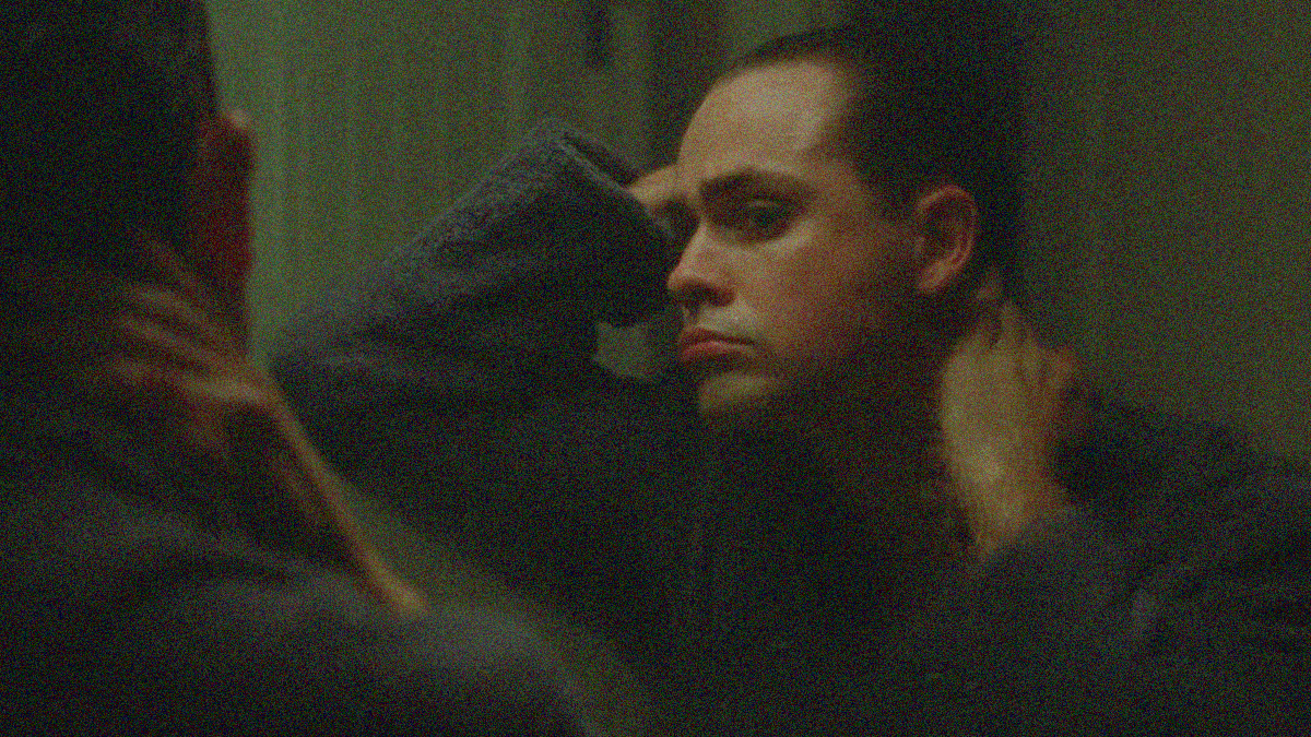 A man cranes and stretches his neck out in a darkened mirror to look at it. We see the reflection.