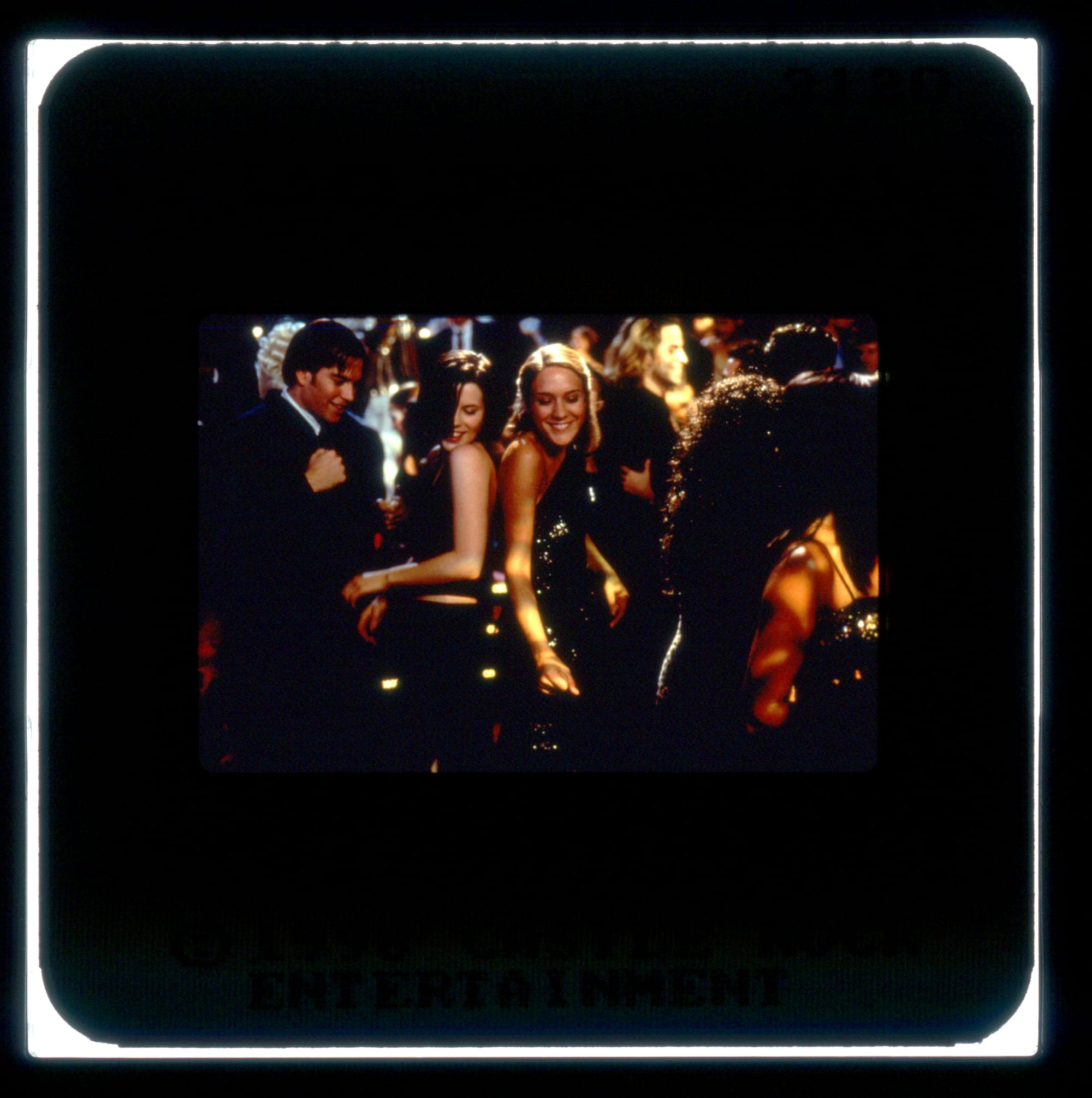 Color Publicity Slide: Two women smiling dance back-to-back in the middle of the frame. A crowd dances around them.