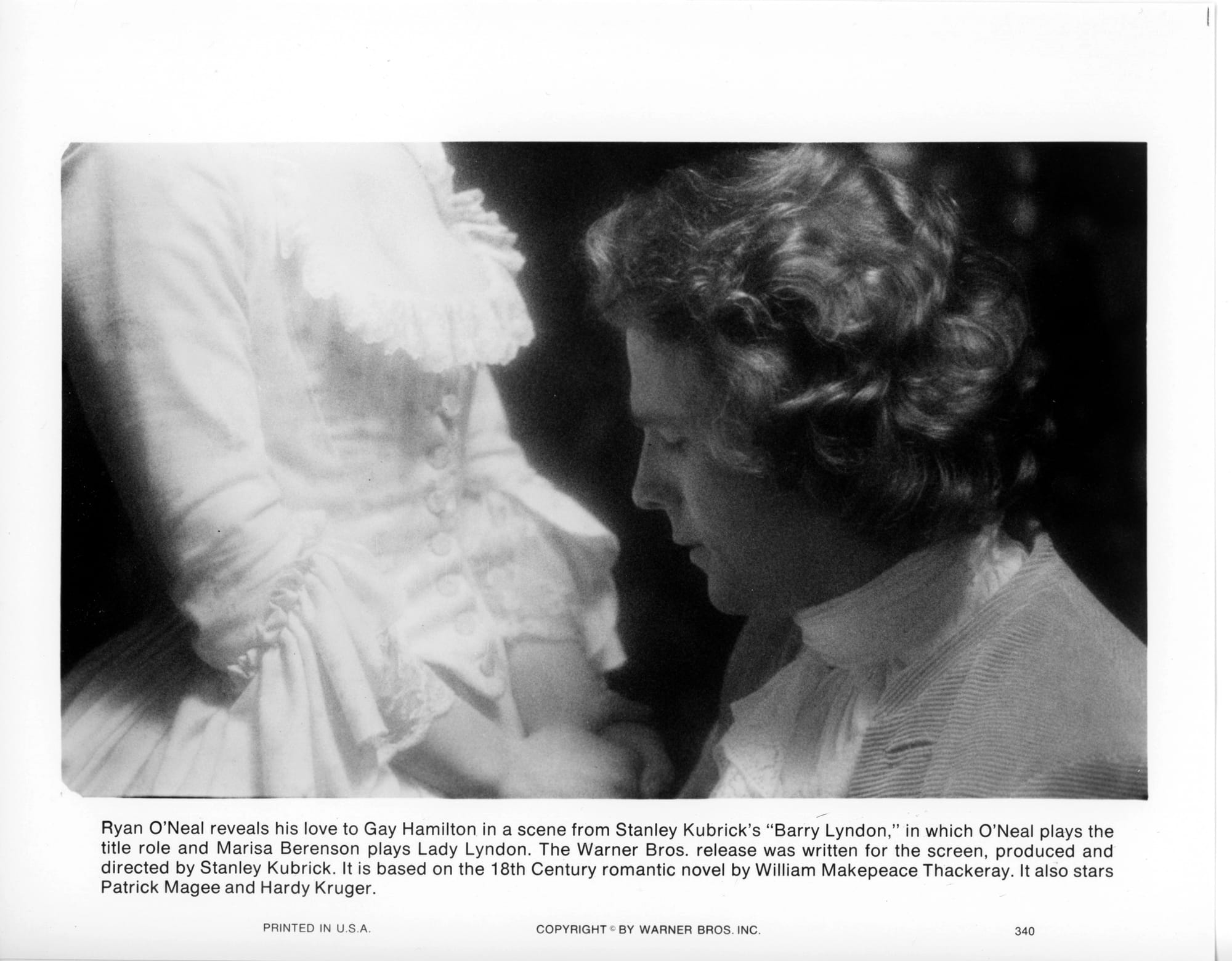 Close-up of a man with wavy hair from shoulders up staring down at the stomach of a woman in white dress (we only see her from chest to hips with hands folded in front of her).