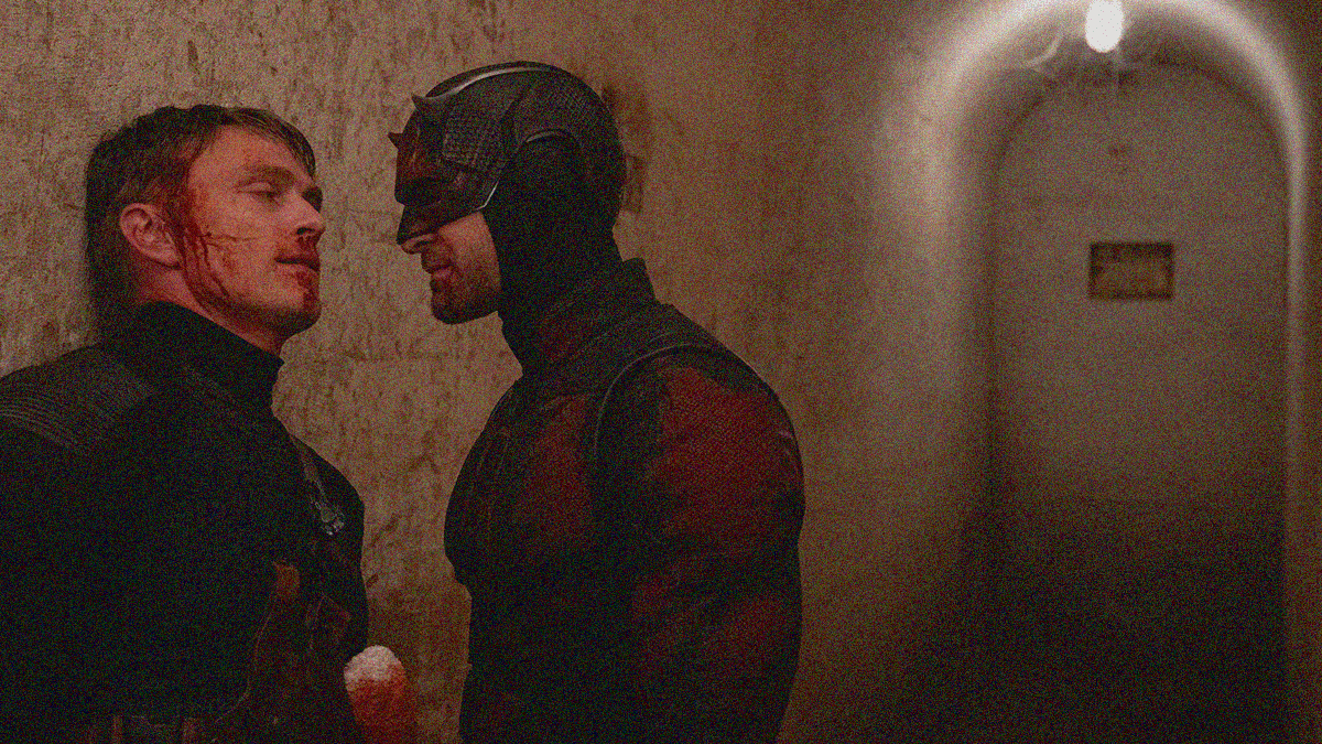 A man with bloodied face is backed against a wall as another in devil superhero costume looms large to block his way.