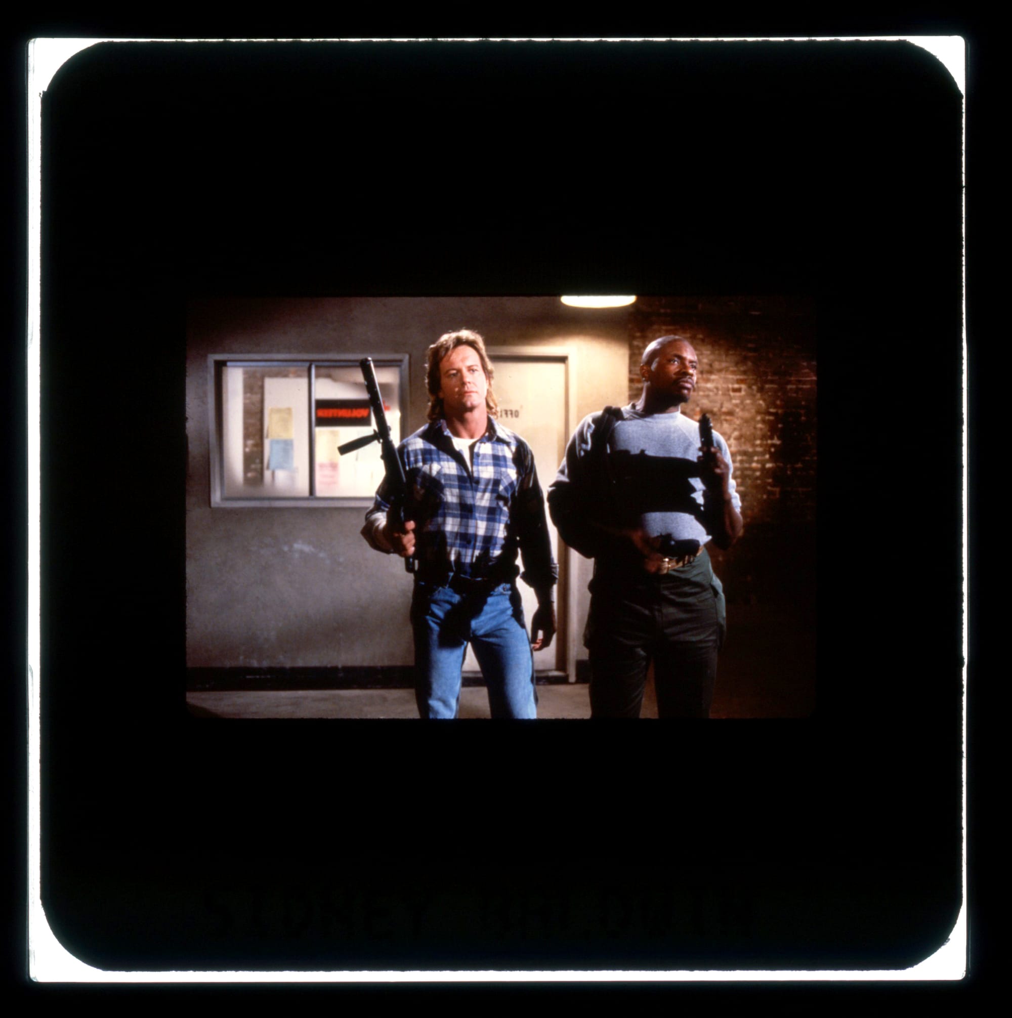 Two men with guns stand outside an office looking tough.