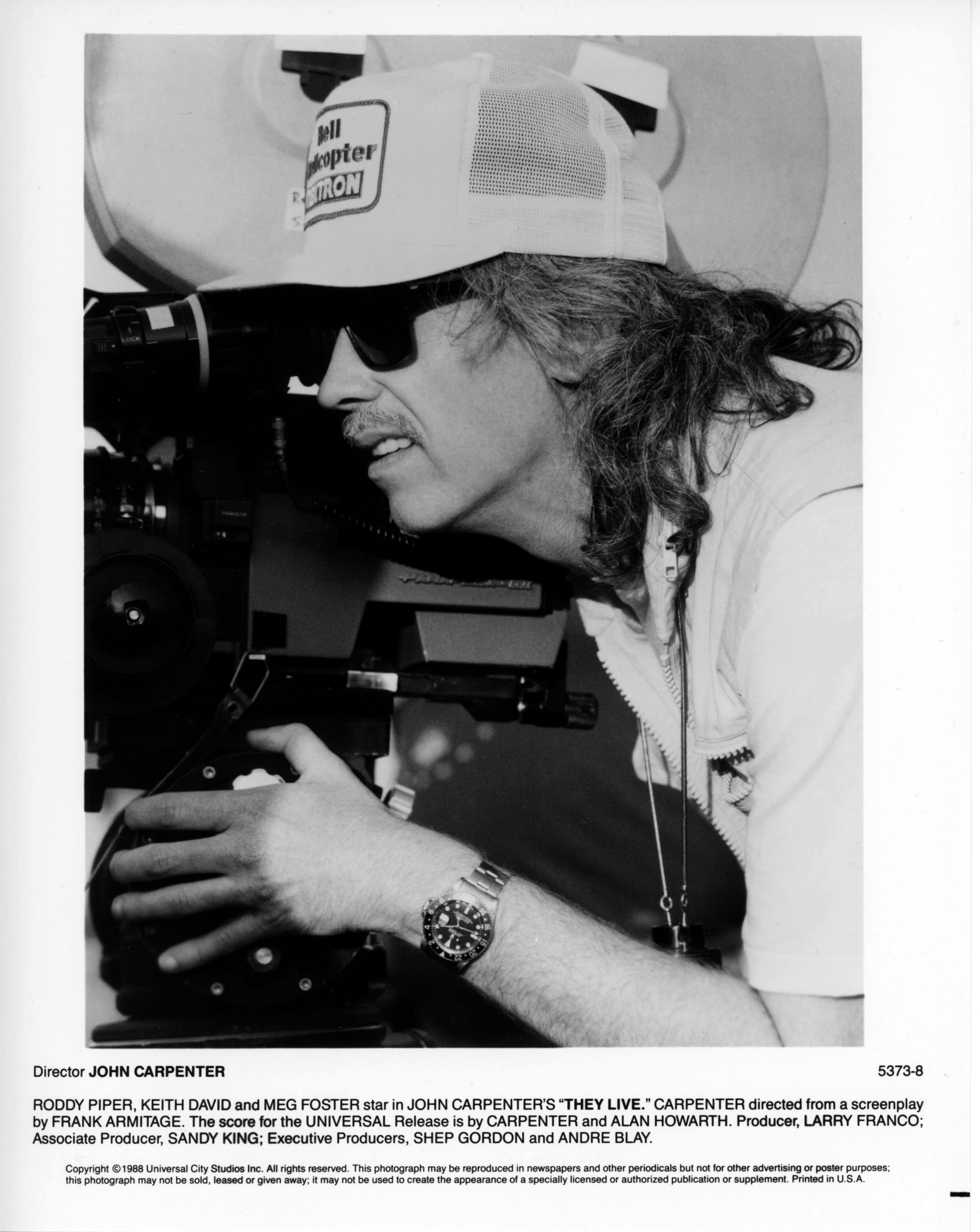 Close-up of a man with sunglasses and a trucker hat peering through the viewfinder of a film camera.