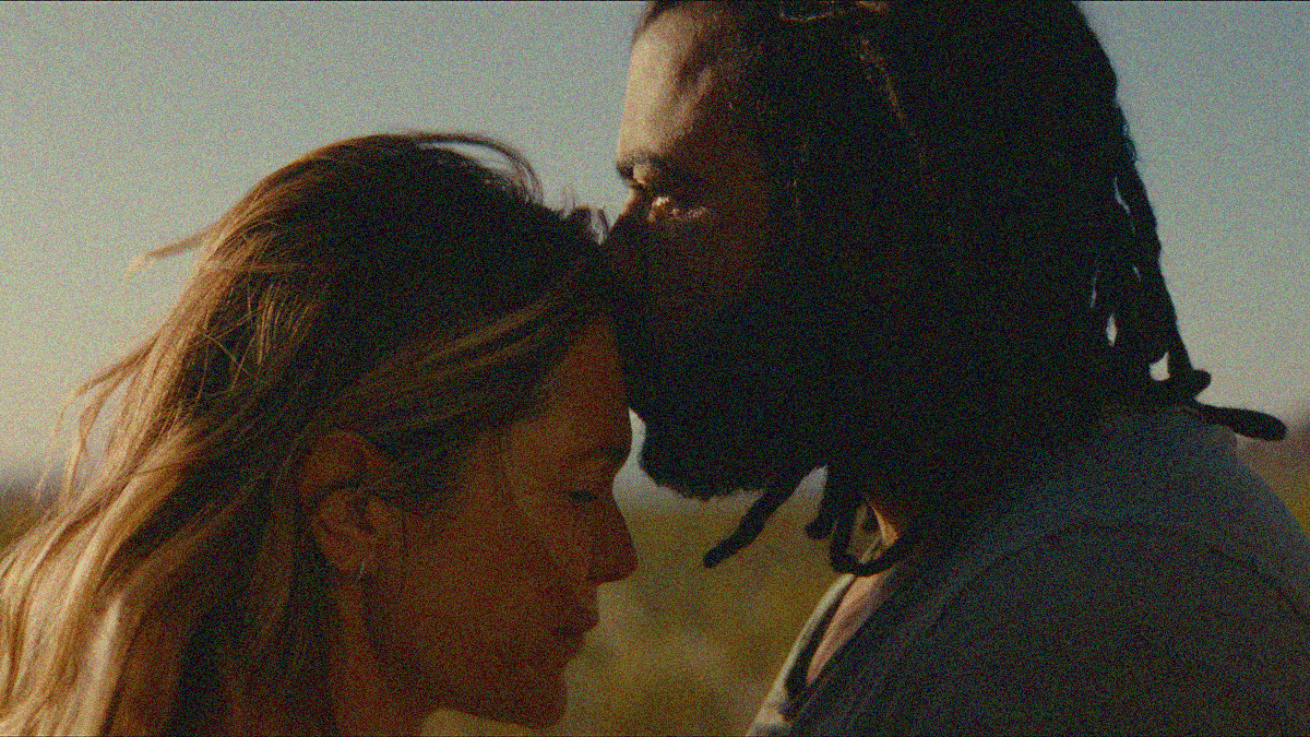 Close-up of a woman and man in profile outside. He is kissing her forehead.