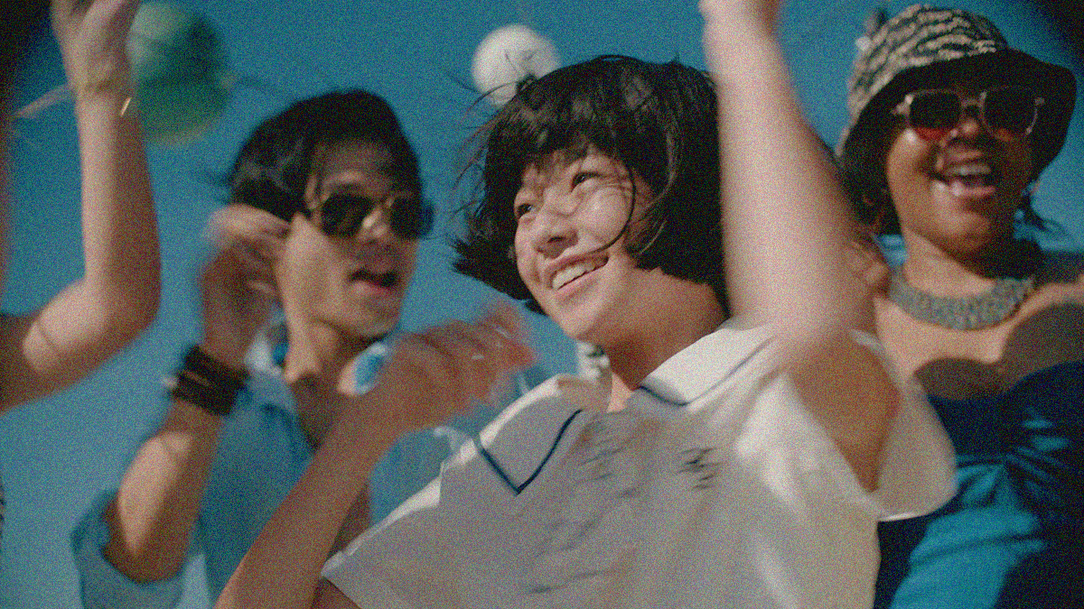A young girl in white is smiling and jumping outside amongst other people dancing.
