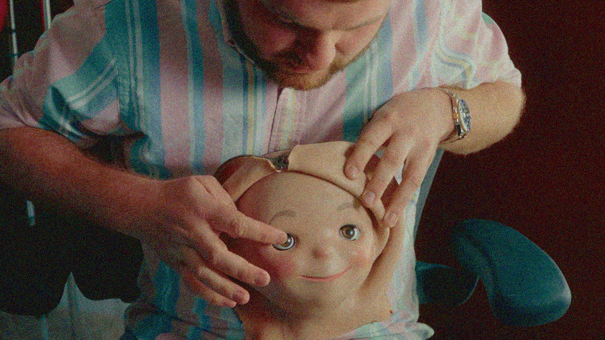 A man is leaning over and manipulating the rubber "skin" of an animatronic head.