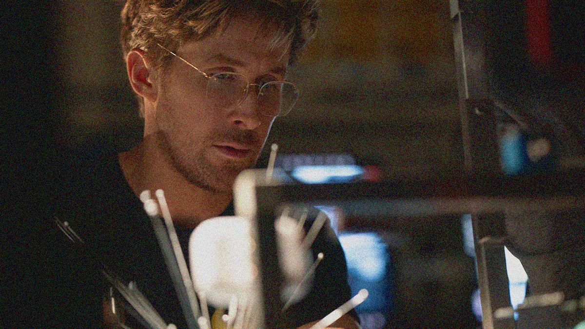 Close-up on a man with glasses seated at a desk and looking at something with metal spikes fanning out from its center.