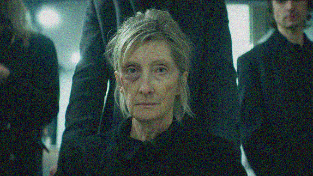 An older woman with a black eye sits in a wheelchair as three people stand behind her.