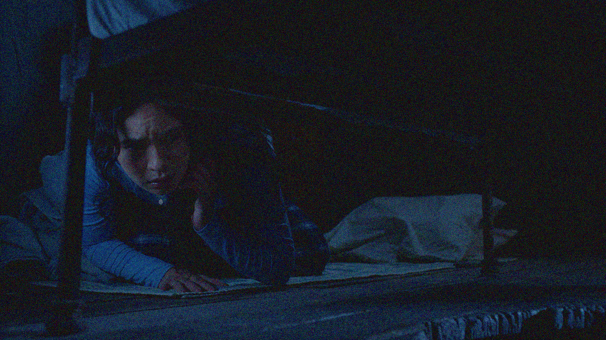 A woman peers under her bed in a darkened room.