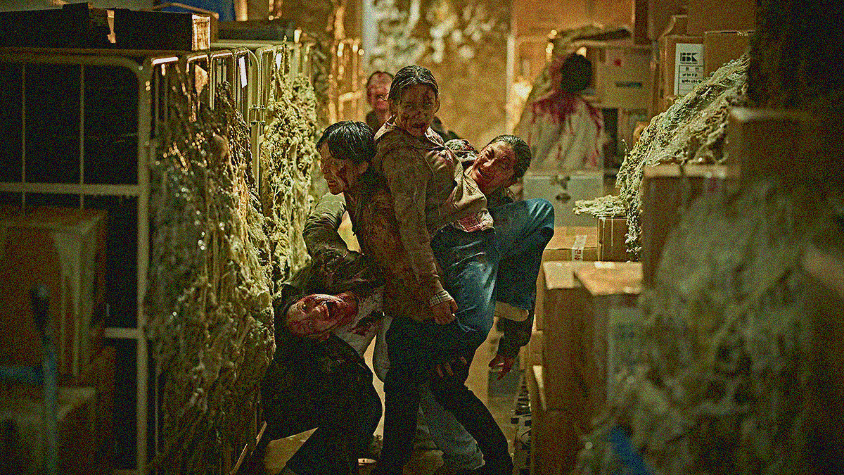 A collection of four "zombies" are contorted and intertwined together in the middle of a fungus-filled hallway looking towards the camera.