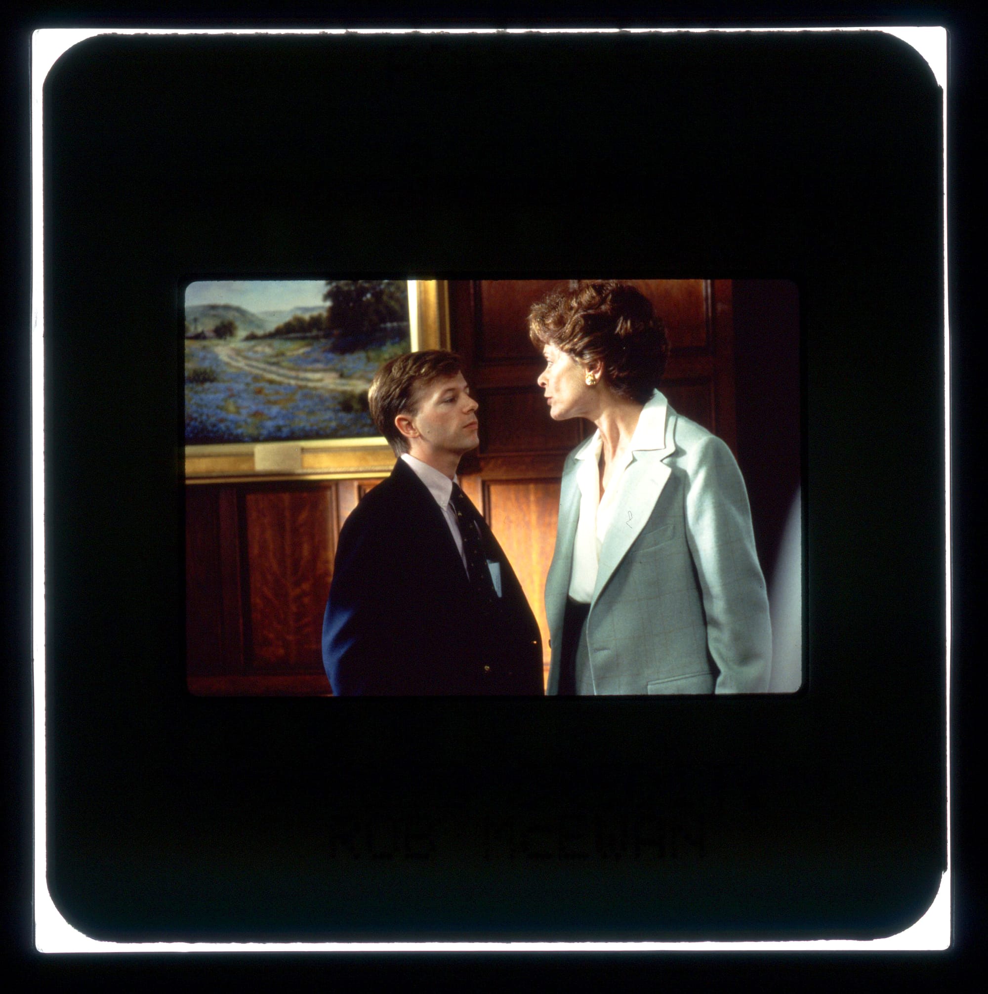 A woman in a blazer is looking down at a man in a suit and tie, chastising him.
