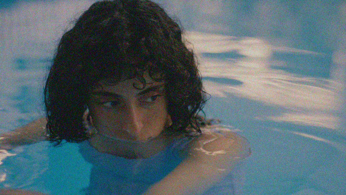 Close-up of a woman in a pool, her body is below the water with her face from the top lip up held above it. She's looking downward and off-screen right.