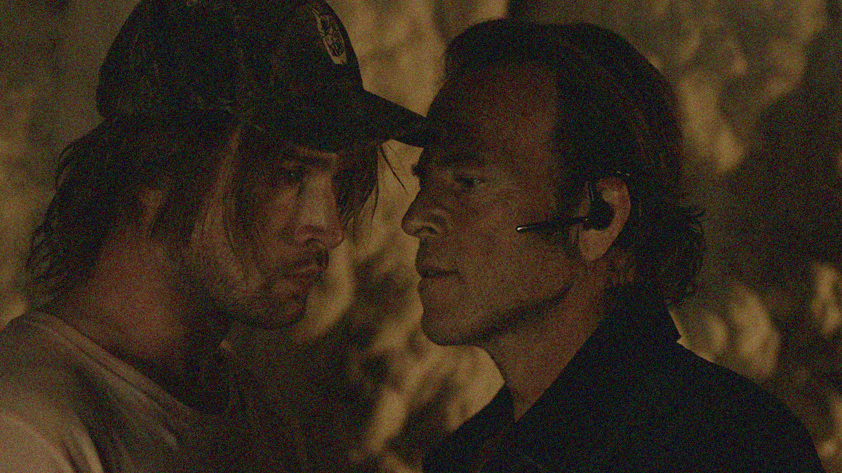 Close-up of two men. The one on the left in ball cap is looking off into the distance. The one on the right is in his face with a scowl.