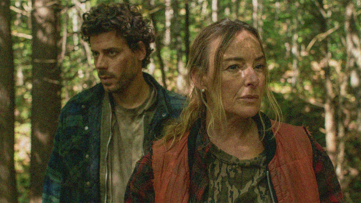 Close-up of a man (on left looking left) and woman (on right looking right) walking through a forest.