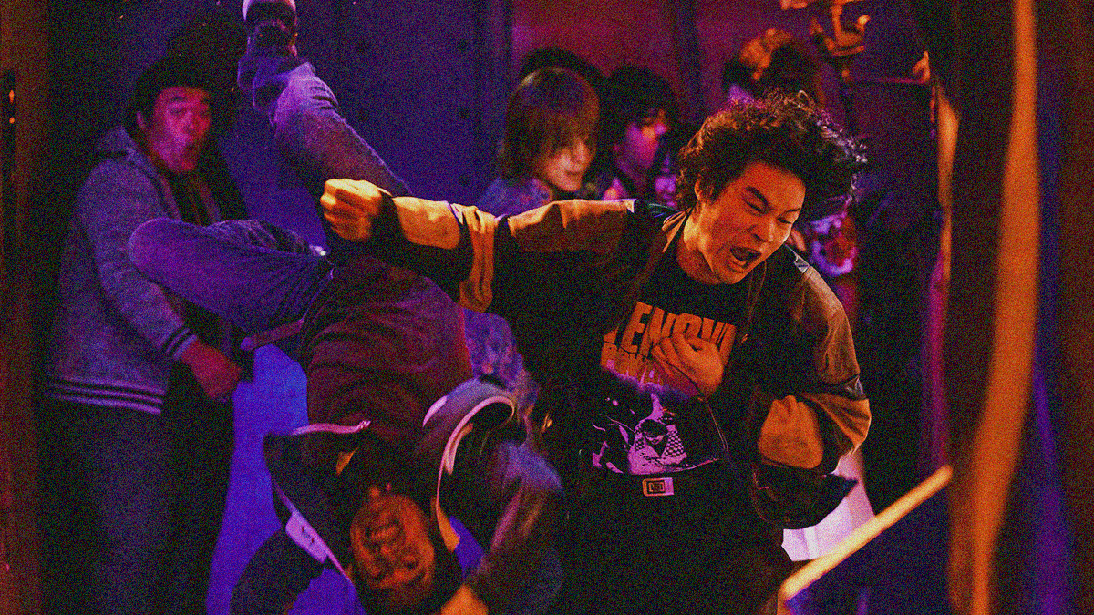 A man with big hair screams as he finishes his clothesline of another man. His victim is literally suspended in the air upside down as a result.