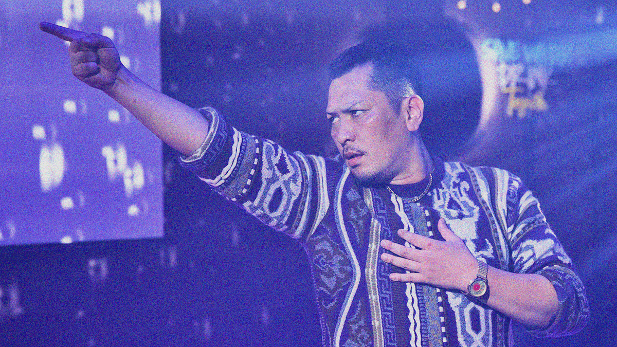 A man from waist up posing with a dance move that has one arm extended outward and his index finger pointed out. You can see the lights of a mirror ball on the walls.