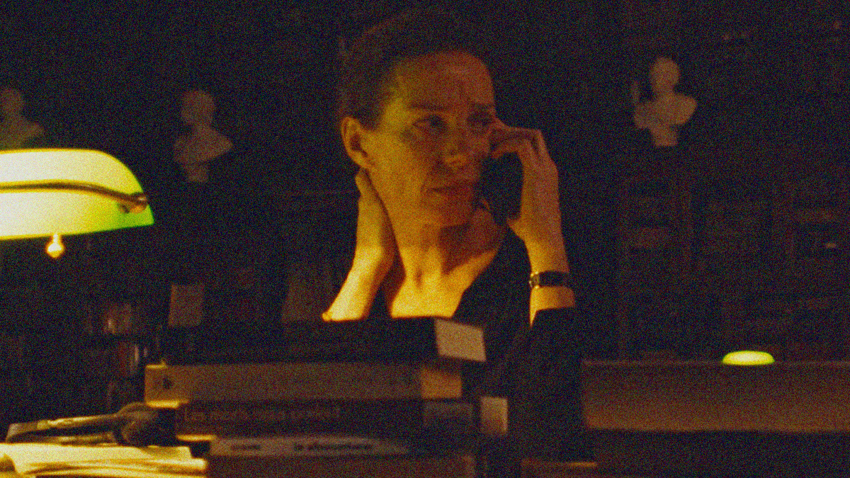 A woman is seated behind a desk of books with a cellphone to her ear.