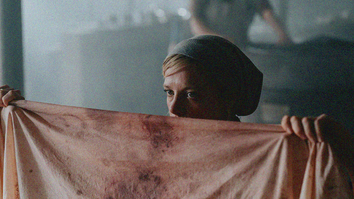 A woman's face from nose up is seen poking up from behind the bloody sheet she holds up in front of her body.