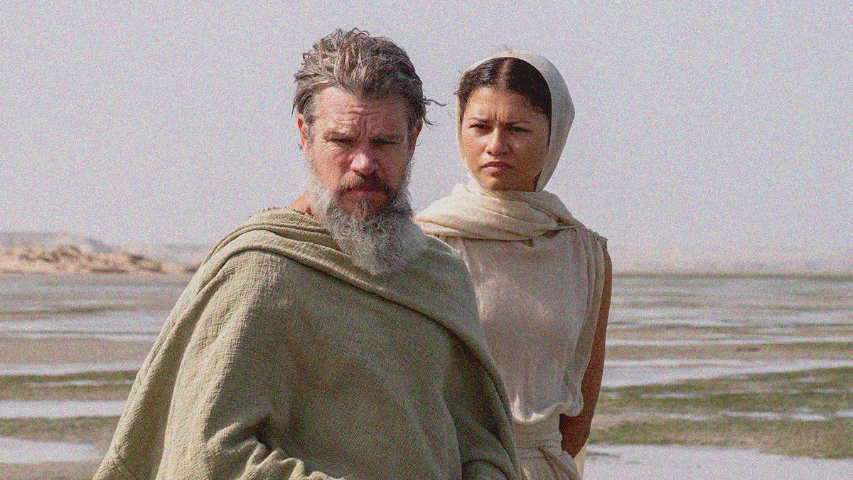 A gray-haired, bearded man in a tunic-like cloak stands besides a young woman in similarly plain clothing with hair covered. A beach of water is seen behind them.
