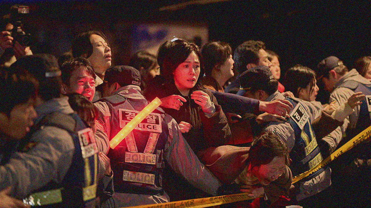 A distraught woman is centered within a night scene amidst a mass of police officers and screaming parents being kept at bay by caution tape.