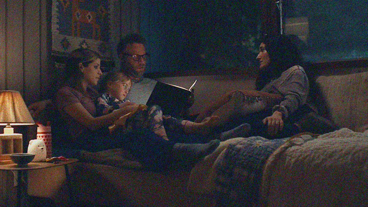 A man and woman read a book to a young girl while another woman watches from the other side of the couch.