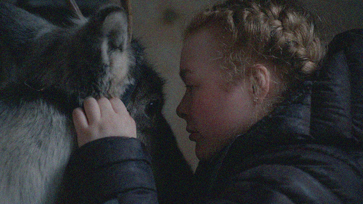 Close-up of a young woman (at right) petting and looking into the eye of a reindeer (at left).