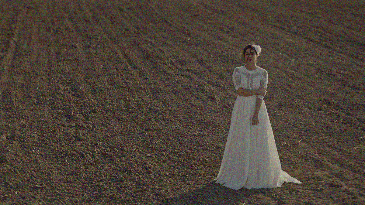 A woman in a wedding dress stands in a field of dirt.
