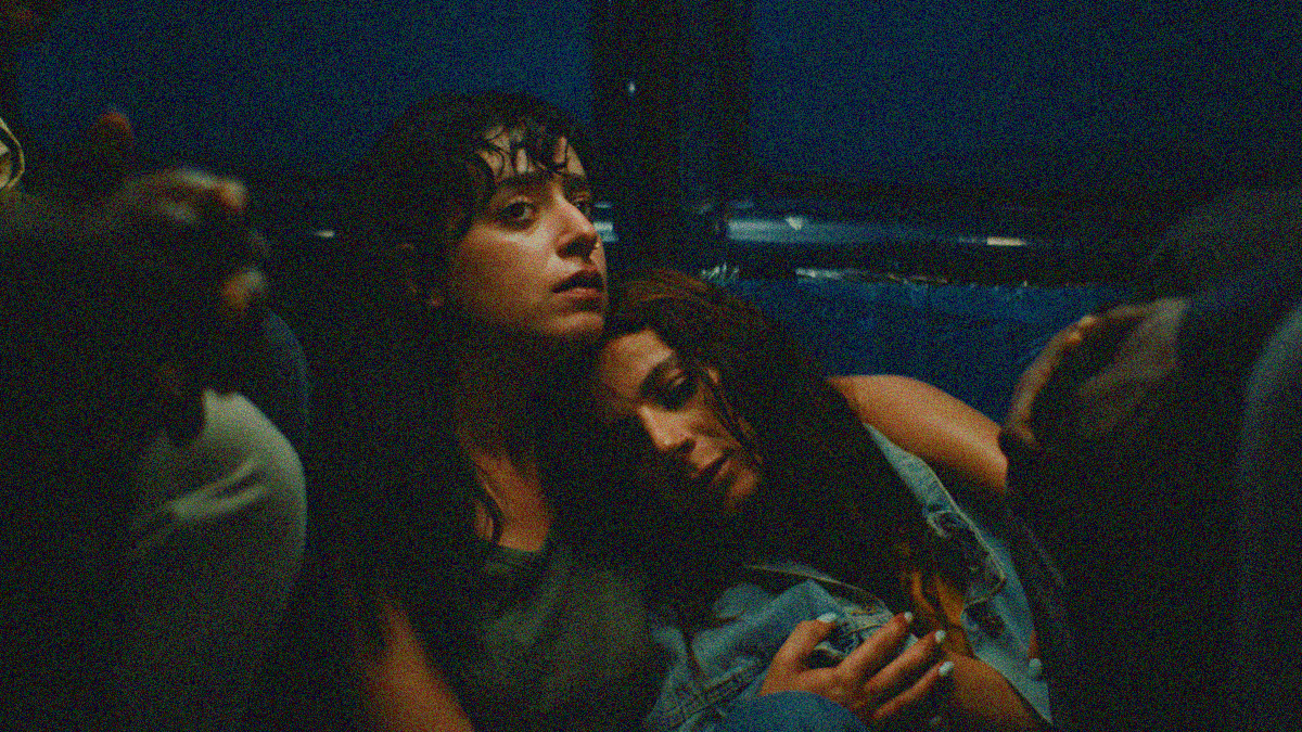 Two tired and scared women as seated at the back of public transportation vehicle, the one's head lays on the other's shoulder.