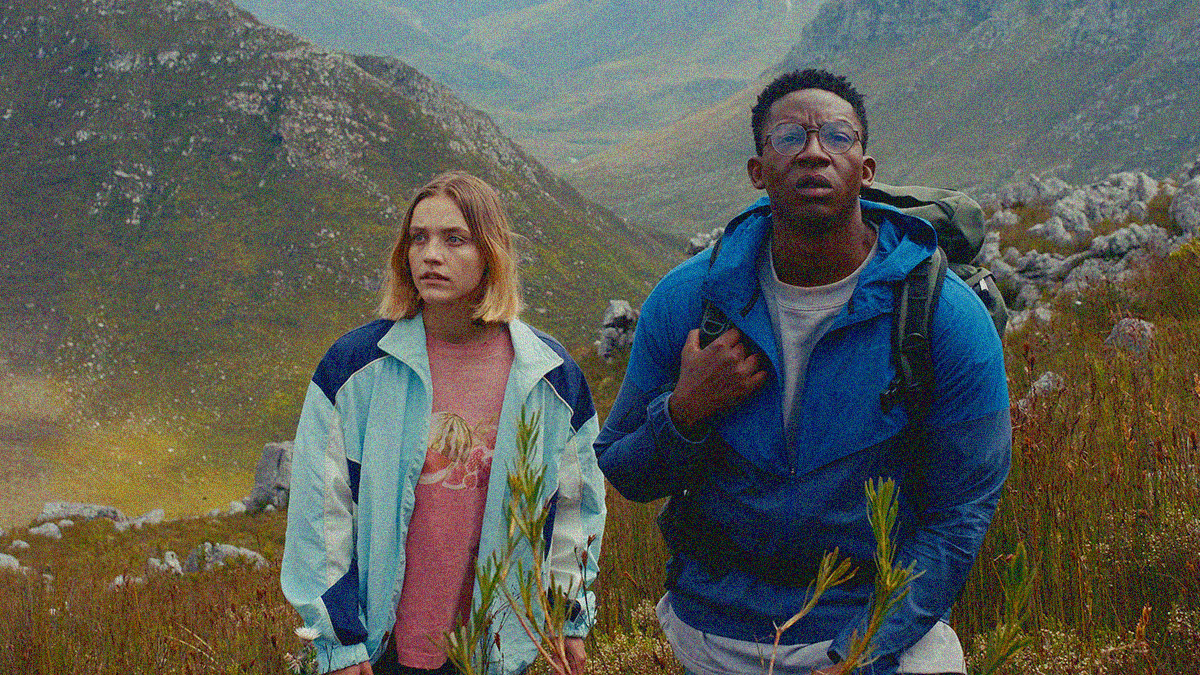 A white woman and Black man stand amidst an expanse of mountains and nature behind them.