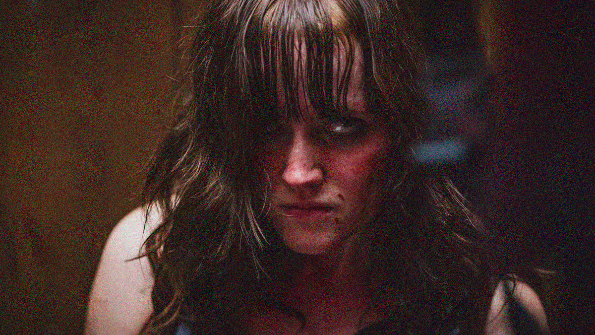 Close-up of a woman with blood on her face looking pissed off at someone off-screen in the foreground.