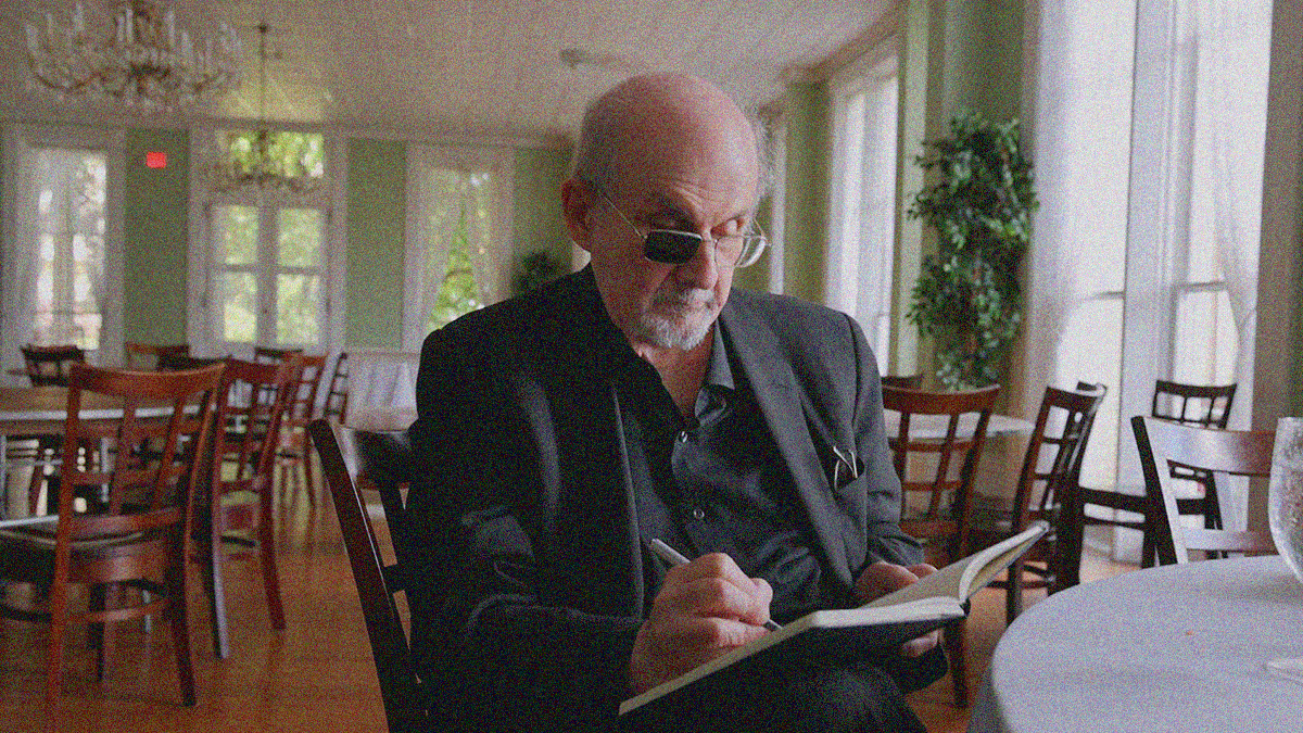The author in a suit and sitting in an empty dining room, writing in a notebook.