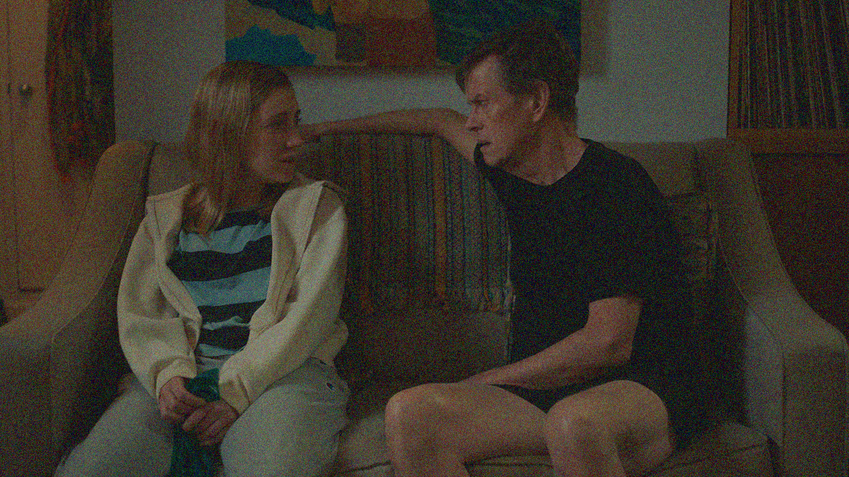 A woman (left) and man (right) sit on a couch, looking at each other in conversation.