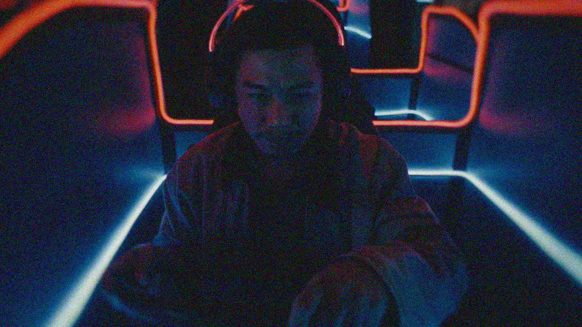 Close-up of a man holding a steering wheel inside a cubicle lit with neon lighting.