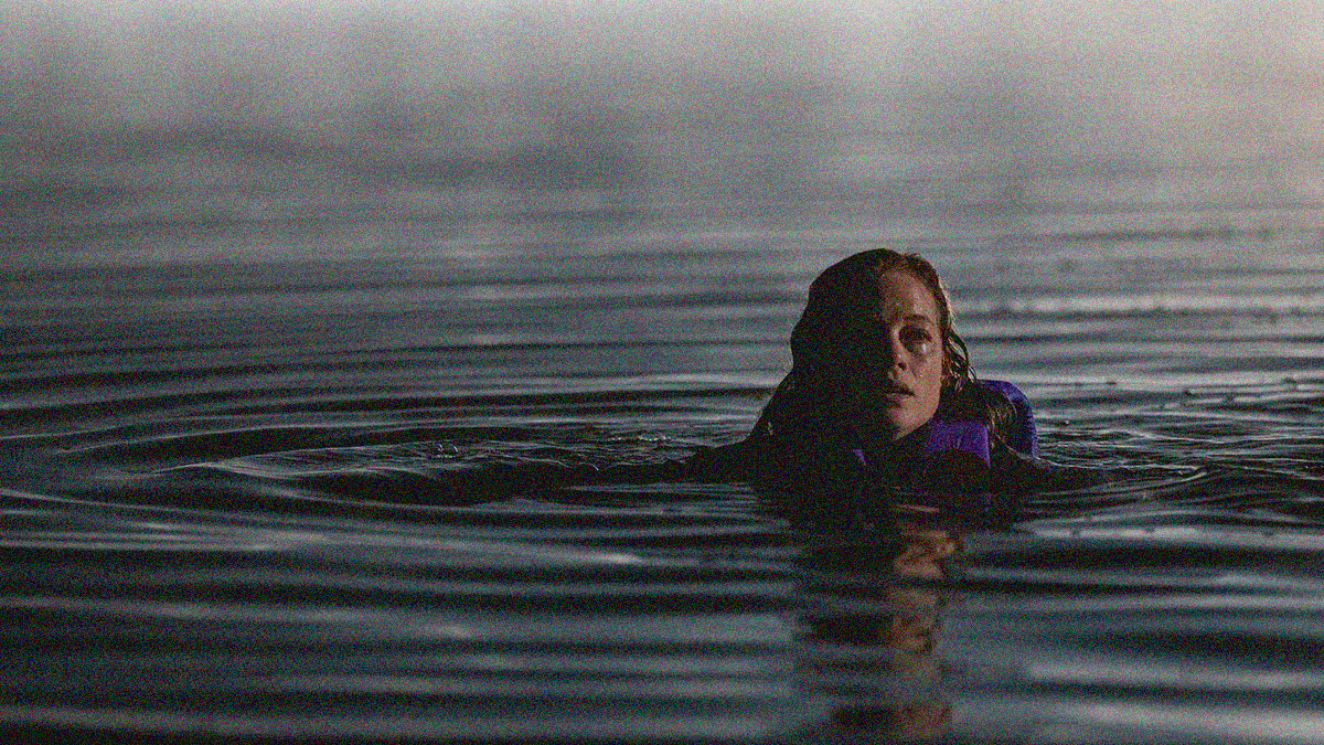 A woman in a blue life jacket is treading water with no land to be seen.