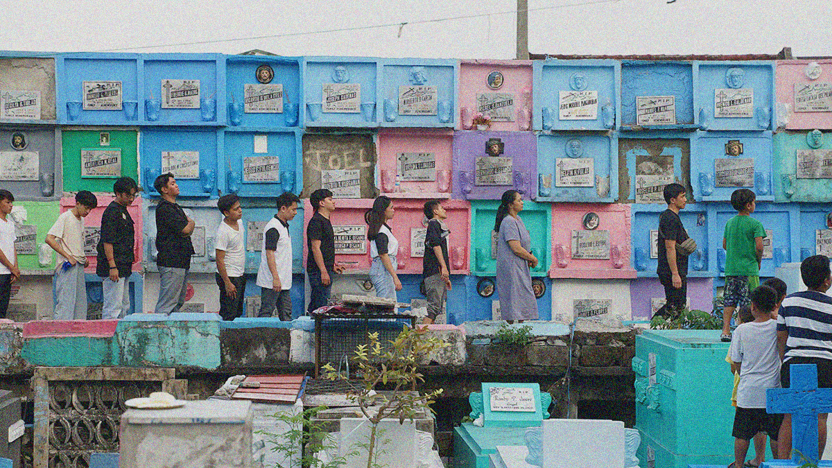 A line of people face right as they walk through a cemetery as part of a funeral procession.