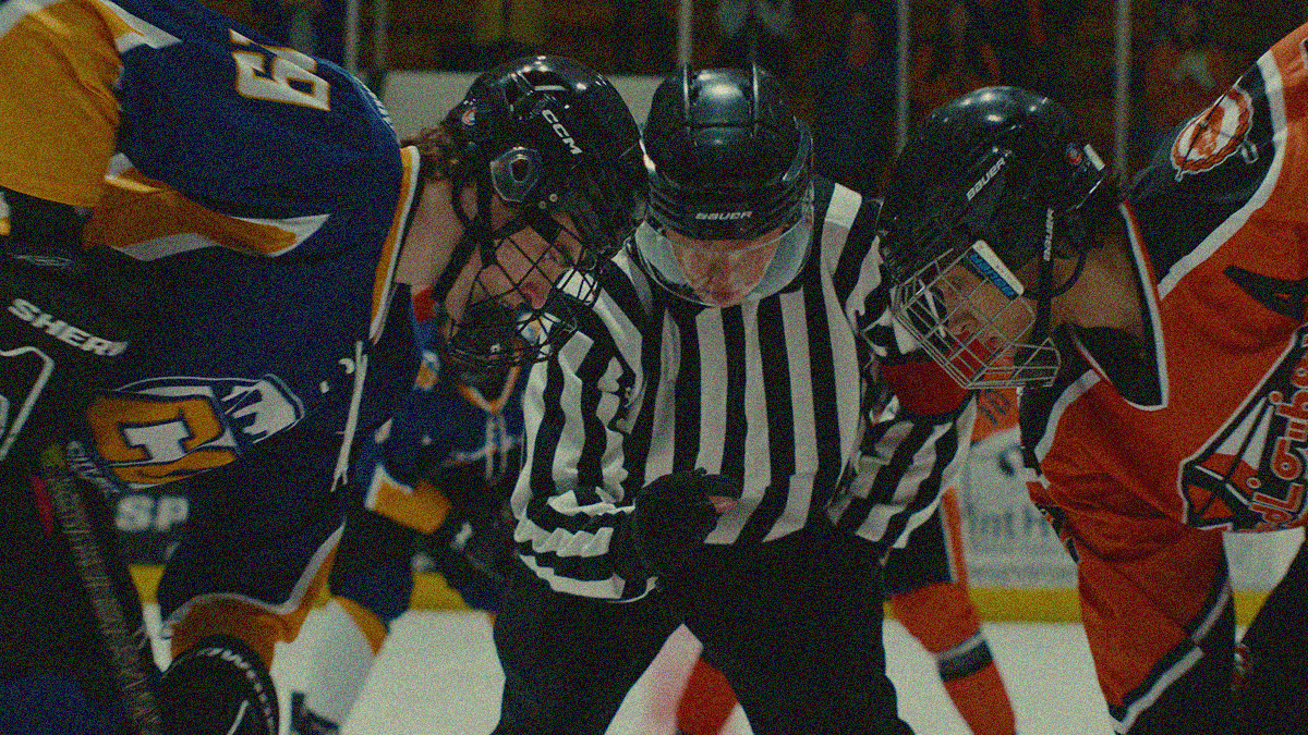 Close-up of a hockey face-off with a player on either side and a referee centered between them.