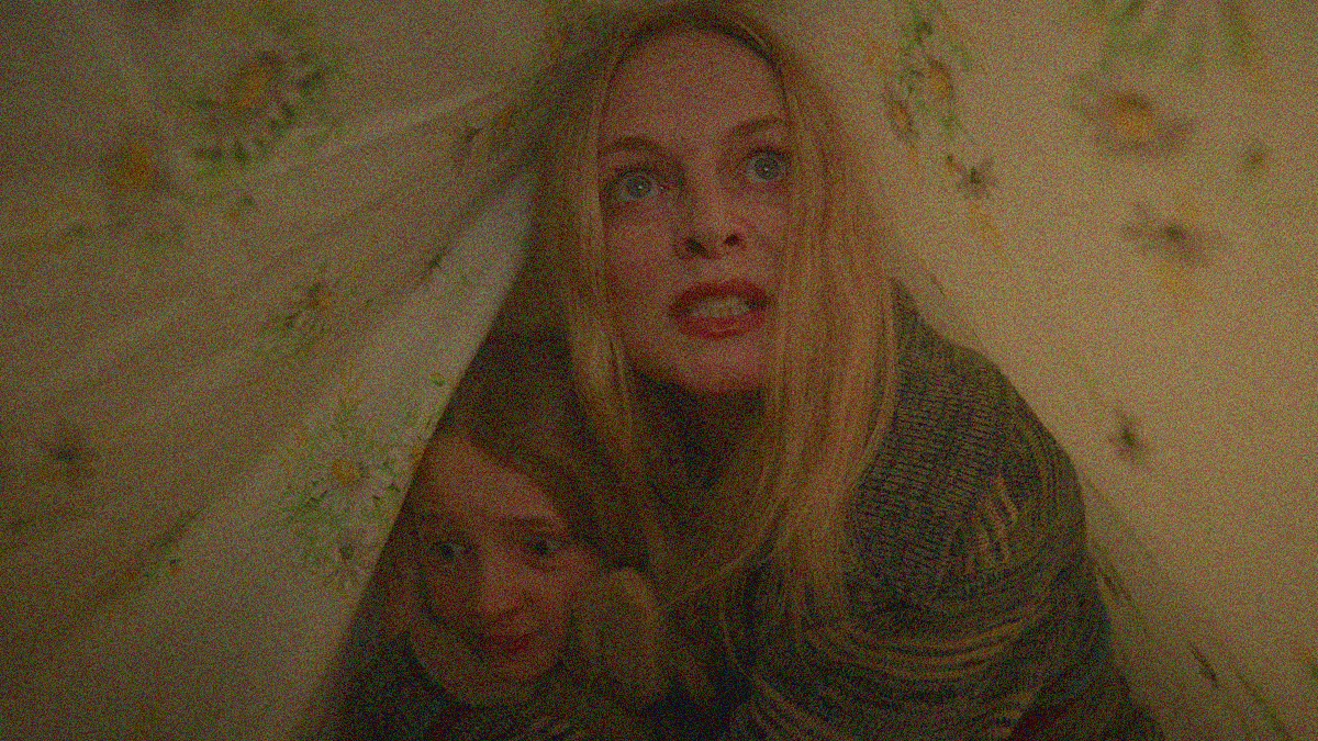 A woman and a child are seen huddled together and angry/scared beneath a sheet.