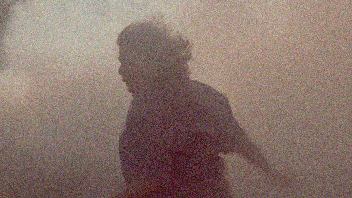 A distressed woman in motion running and turning back. She almost becomes a silhouette in the heavy smoke filling the frame.