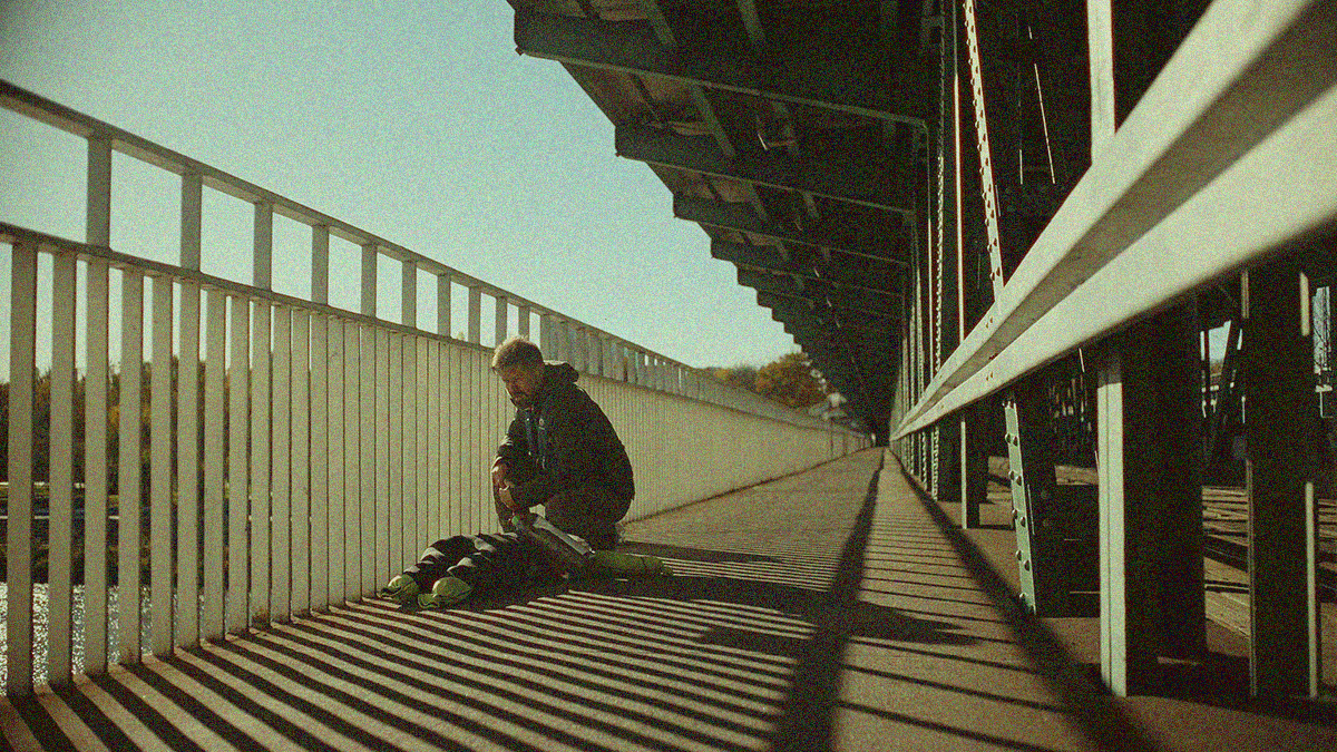 A man on a bridge crouches over a clothed dummy.
